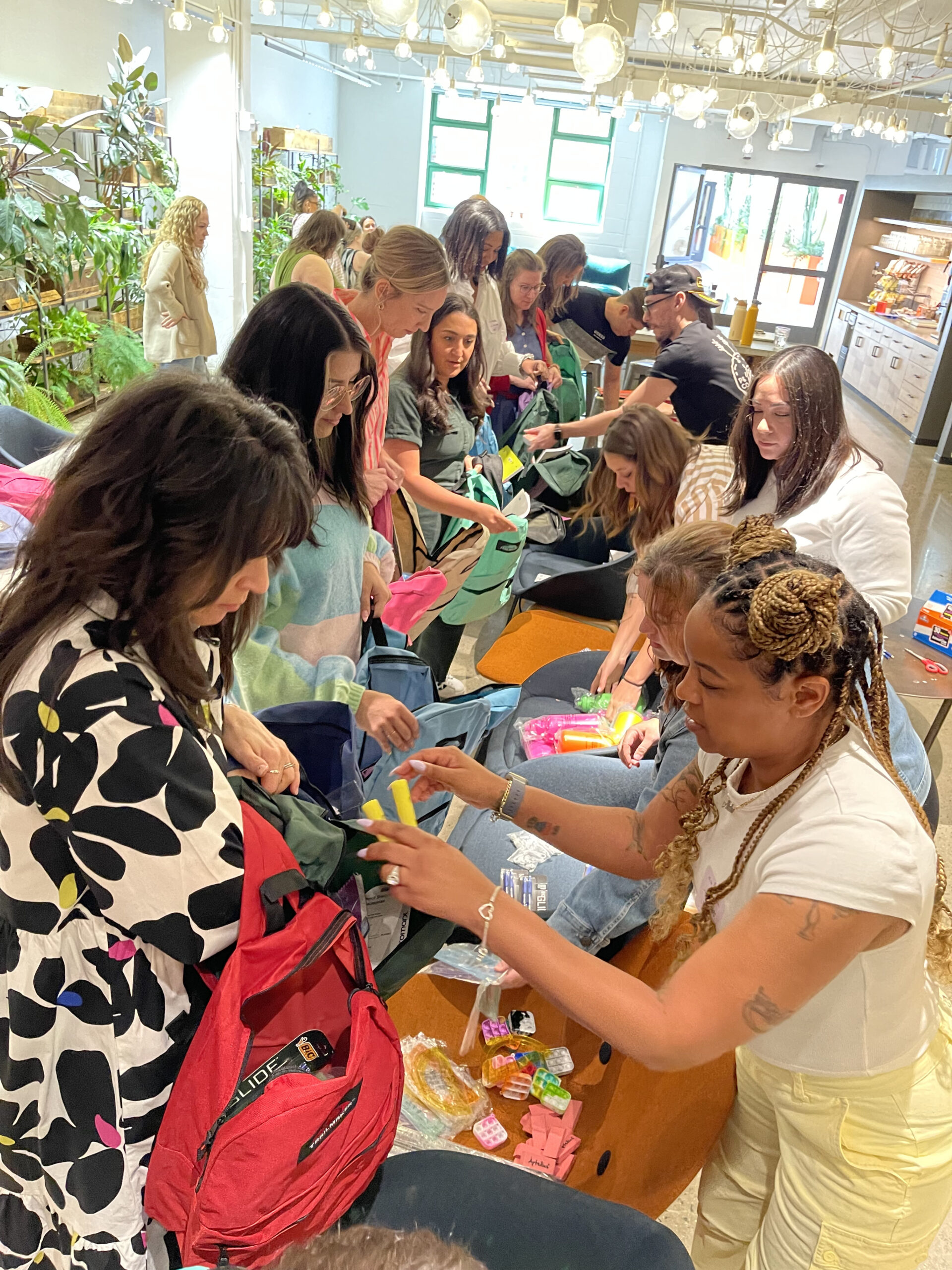 Participants in the 'Tools for Schools' event working together to fill backpacks with essential school supplies such as highlighters, notebooks, and pencils.