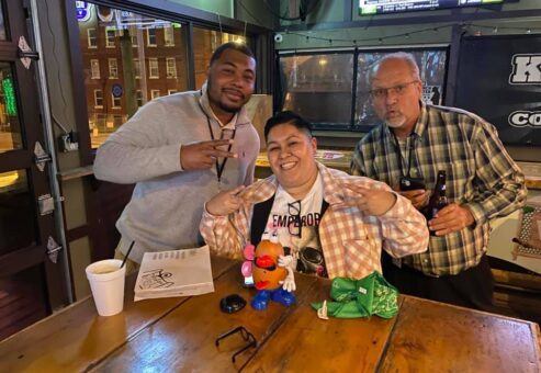 Team enjoying their Pub Crawl Scavenger Hunt, posing with playful props at a local bar, showcasing teamwork and camaraderie during the fun-filled event.