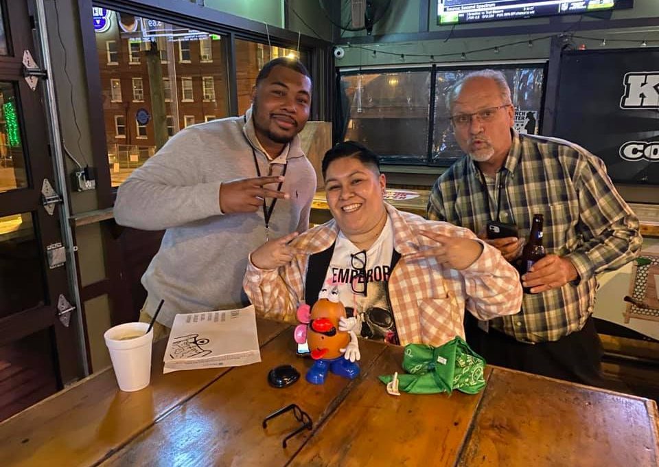 Team enjoying their Pub Crawl Scavenger Hunt, posing with playful props at a local bar, showcasing teamwork and camaraderie during the fun-filled event.