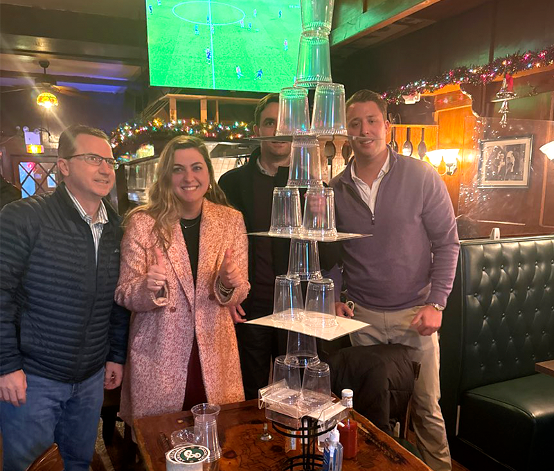 A group of team members proudly displaying their impressive tower of stacked cups during the Pub Crawl Scavenger Hunt, showcasing creativity and teamwork in a lively bar setting.