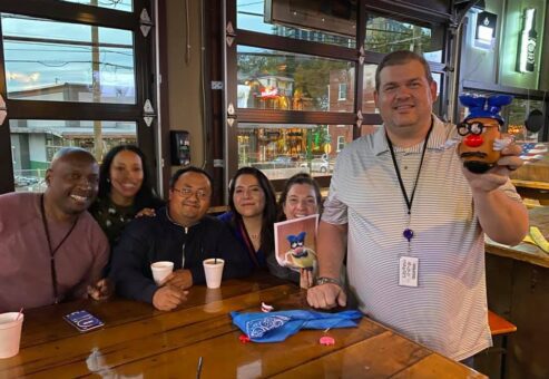 A cheerful group of colleagues enjoying the Pub Crawl Scavenger Hunt, proudly showing off their creative achievements as part of the fun and camaraderie building event.
