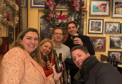 Smiling team members raise their drinks in celebration during a festive stop on the Pub Crawl Scavenger Hunt, enjoying the holiday decor and camaraderie.
