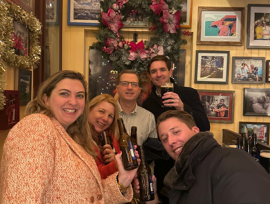 Smiling team members raise their drinks in celebration during a festive stop on the Pub Crawl Scavenger Hunt, enjoying the holiday decor and camaraderie.
