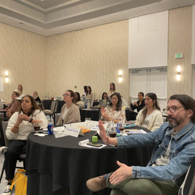 Participants attentively listen and engage during a board-breaking team building event, preparing to overcome personal and professional barriers. thumbnail