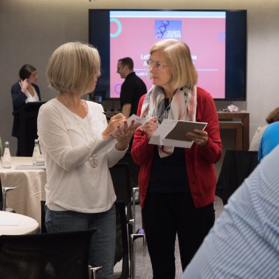 Two participants discussing and exchanging ideas during a Team DNA or Leadership DNA session, with other attendees engaged in the background. thumbnail
