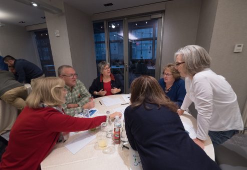 A group of participants collaborating at a table during a Team DNA workshop, discussing and working on materials with a facilitator nearby.