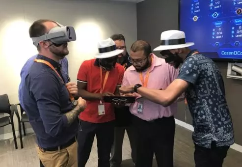 A team of participants in The Infinite Loop team building event collaborates, with some wearing VR headsets and others observing, working together to solve a virtual challenge.