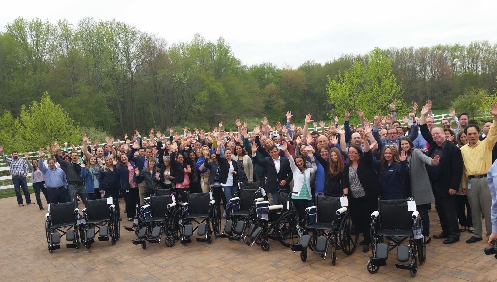 A bunch of people standing behind wheelchairs cheering and waving their hands