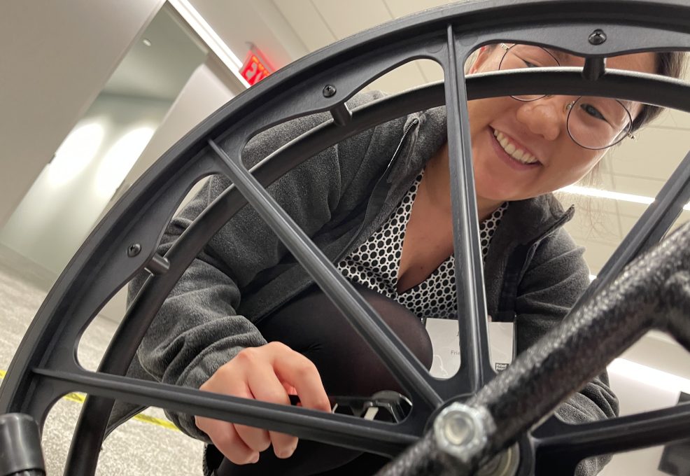 A participant smiles while working on assembling a wheelchair during a team building event for charity. The Wheelchairs In Motion activity involves building wheelchairs to donate to veterans and those in need.
