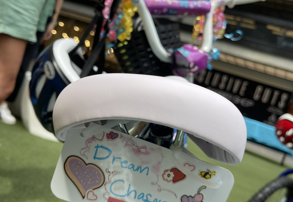 Close-up of a decorated bicycle from a Charity Bike Build event. The bike seat features a personalized tag reading 'Dream Chaser' with colorful stickers, including hearts, a cupcake, and motivational text 'Have a Good Day,' showing thoughtful details in the bike assembly process.