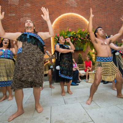 Maori performers in traditional dress energetically lead a Haka team building session, inspiring participants with chants and powerful movements. thumbnail