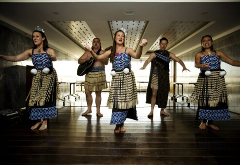 Maori performers in traditional attire deliver an energetic Haka team building experience indoors, showcasing dance, chant, and cultural instruments.