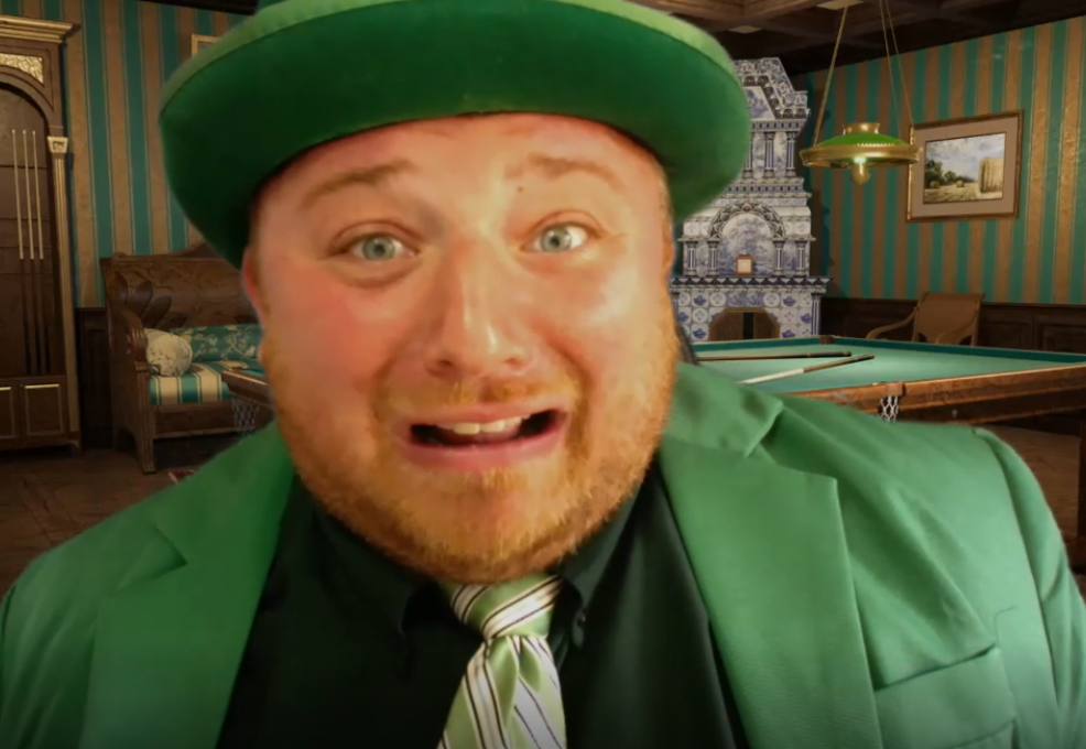 A man wearing a bright green suit, green tie, and matching green hat is seen in the foreground with an exaggerated, nervous expression on his face. The man’s expression and vivid outfit create a humorous and lively atmosphere. He's role-playing in a murder mystery team building event.