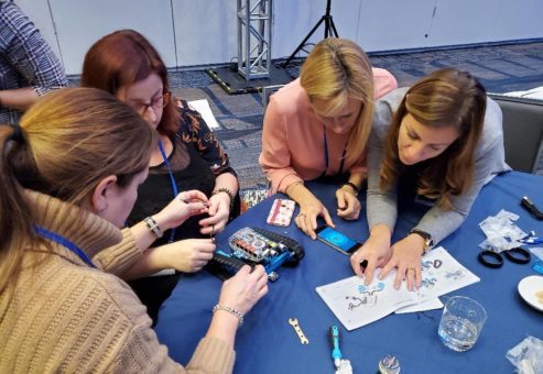 A team of four participants focuses on assembling a robot, using tools and an instruction manual as part of a team building activity. They are seated around a table, collaborating on the technical task.