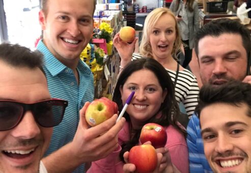 Team posing with apples inside a grocery store during a challenge for the Team-opoly scavenger hunt event.