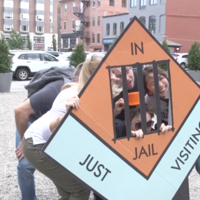 Group posing with a life-sized 'In Jail' game piece during a Team-opoly scavenger hunt team building event. thumbnail
