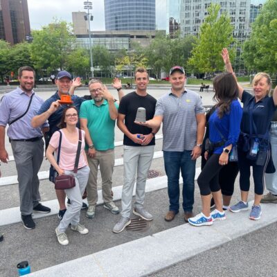 A team of participants smiling and posing in an outdoor plaza during a Team-opoly scavenger hunt team building event. thumbnail