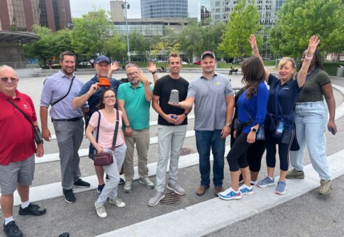A team of participants smiling and posing in an outdoor plaza during a Team-opoly scavenger hunt team building event.