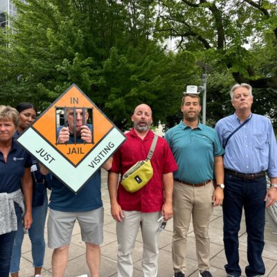 Team posing with a Monopoly-style 'In Jail' prop during a Team-opoly scavenger hunt team building event. thumbnail