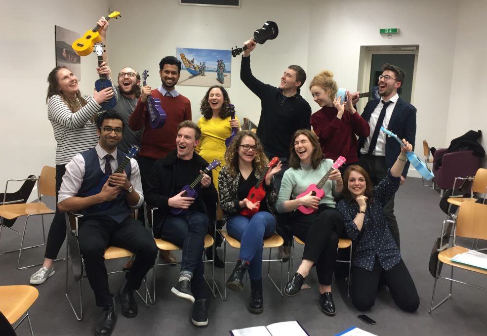 Team building event with participants enthusiastically holding colorful ukuleles. The group is smiling, laughing, and ready to perform, showcasing their creative collaboration during a Team Ukulele music session.