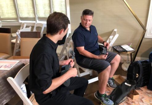 Two participants sitting and holding ukuleles during a team building event. They are engaged in conversation, learning to play their instruments as part of the Team Ukulele music activity.