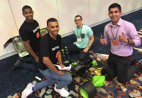 Four individuals kneeling on the floor assembling a Green Machine bike during a team building event. One person gives a thumbs-up while others smile, holding tools and instructions, as they work together on the project.