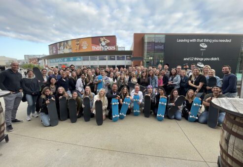 Large group of participants proudly display skateboards they built together during The Mystery Bus team building event, fostering teamwork and creativity.