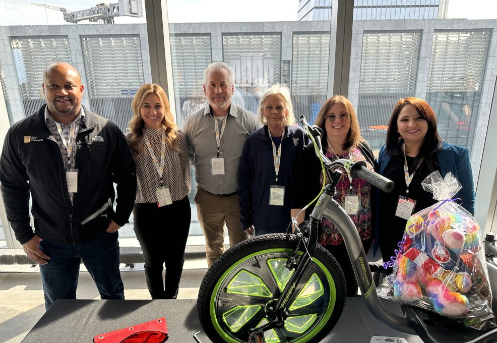 A group of five people standing behind a Green Machine bike with neon green wheels, proudly displaying their efforts for a charitable team building event.