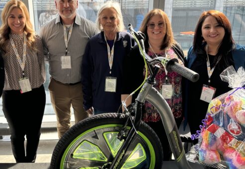 A group of five people standing behind a Green Machine bike with neon green wheels, proudly displaying their efforts for a charitable team building event.