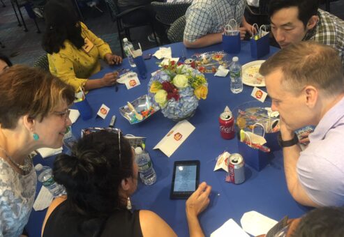 Team members huddle around a table, strategizing answers during a high-energy Corporate Quiz Bowl team building challenge.