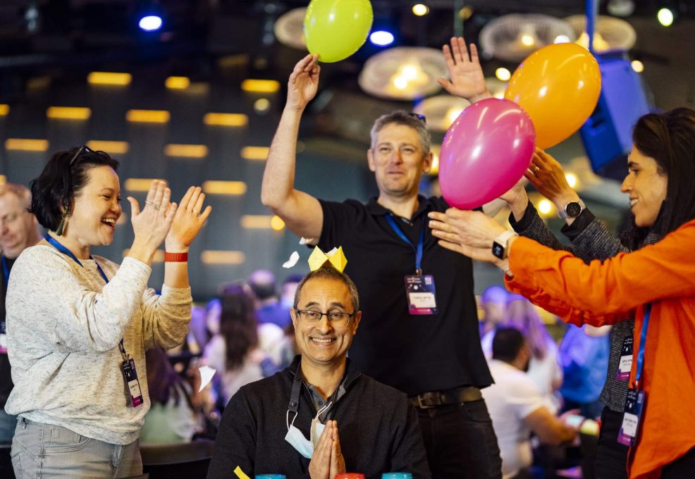 Participants are enthusiastically engaging with balloons as part of a creative challenge, working together to rack up points. The energy is high, and everyone is immersed in the fun, showcasing teamwork and leadership skills!