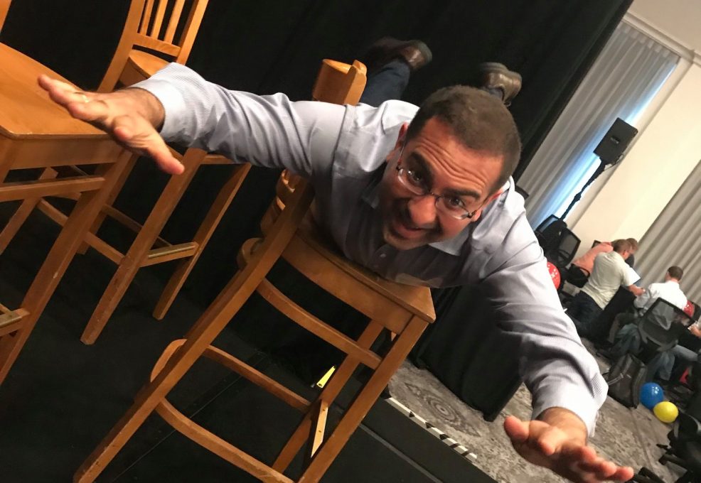 A participant fully embraces the fun and physical aspect of the game, executing a dramatic chair stunt while surrounded by a team engaged in the lively atmosphere. This highlights the playful, energetic spirit of the event.