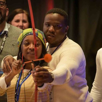 A group of participants focus intently while aiming a bow and arrow during a team building event, demonstrating their teamwork and precision. thumbnail