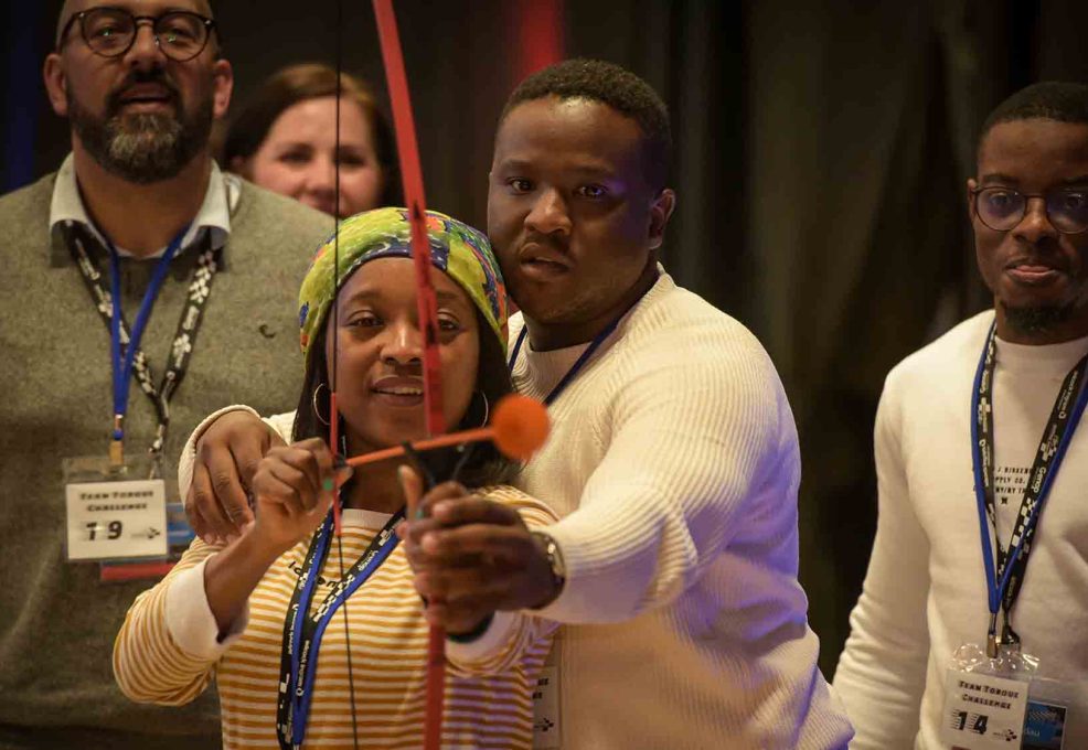 A group of participants focus intently while aiming a bow and arrow during a team building event, demonstrating their teamwork and precision.