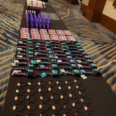 Tables lined with carefully arranged essential items, including brushes and personal care products, ready to be packed into handbags for donation during the Hopefull Handbags Global team building event. thumbnail