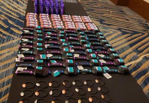 Tables lined with carefully arranged essential items, including brushes and personal care products, ready to be packed into handbags for donation during the Hopefull Handbags Global team building event.