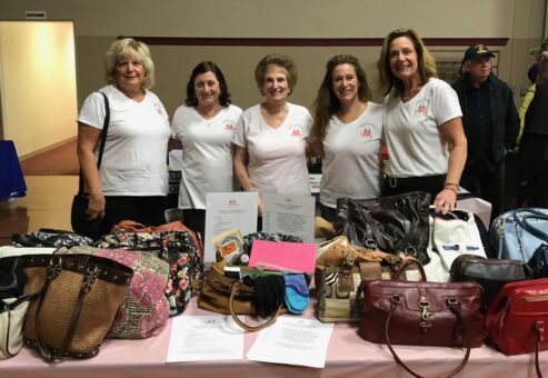 Participants proudly display filled handbags during the Hopefull Handbags Global team building event, supporting survivors of domestic abuse with essential items and hope.
