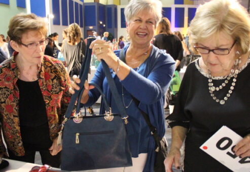 Participants selecting handbags for donation during a Hopefull Handbags Global team building event, supporting survivors of domestic abuse with essential items and hope.