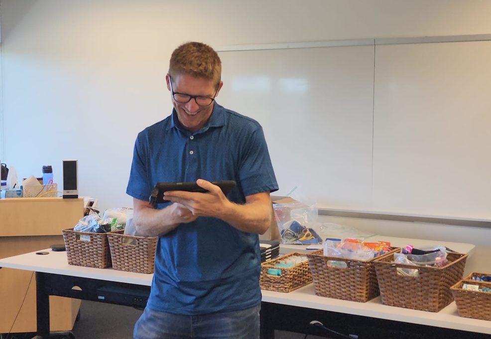 Participant smiling during a Hopefull Handbags Global team building event, where baskets of essential items are ready to be packed into handbags for donation to women survivors of domestic abuse.