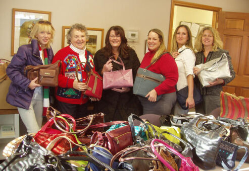 Participants proudly display gently-used handbags collected for donation at a Hopefull Handbags Global team building event, supporting survivors of domestic abuse.
