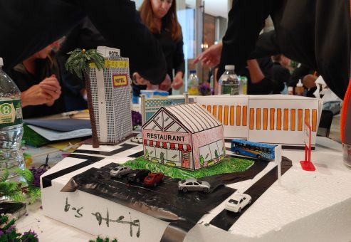 Close-up of a miniature city model featuring a restaurant, hotel, parking lot, and roadway, created during a City Build team building activity.