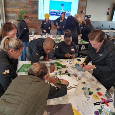 Team members collaborating on a City Build team building project, working together to construct miniature city zones using materials, models, and creative elements. thumbnail
