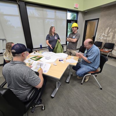Team members collaborating at a table during the City Build team building event, planning their miniature city model with materials and blueprints. thumbnail