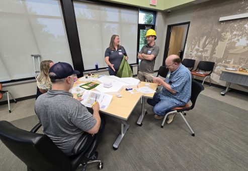 Team members collaborating at a table during the City Build team building event, planning their miniature city model with materials and blueprints.