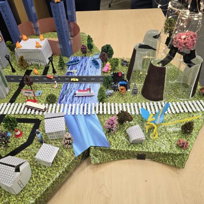 Close-up of a detailed miniature city model featuring buildings, roads, trees, and waterways created during the City Build team building event. thumbnail