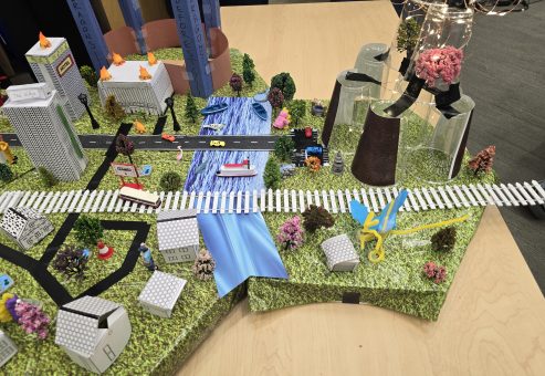 Close-up of a detailed miniature city model featuring buildings, roads, trees, and waterways created during the City Build team building event.