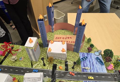 Creative city model with labeled towers, roads, waterways, and miniature vehicles, showcasing teamwork from the City Build team building event.