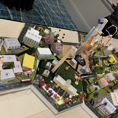 Colorful and detailed miniature city model created during a City Build team building event, featuring buildings, roads, trees, and decorative lights. thumbnail