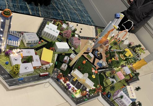 Colorful and detailed miniature city model created during a City Build team building event, featuring buildings, roads, trees, and decorative lights.