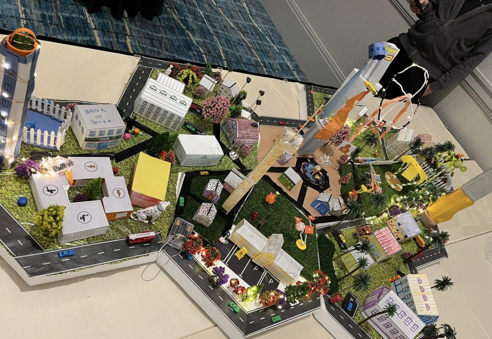 Colorful and detailed miniature city model created during a City Build team building event, featuring buildings, roads, trees, and decorative lights.